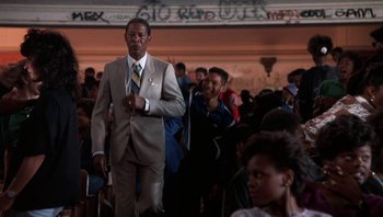 Movie still from “Lean on Me” (1989), directed by John G. Avildsen – A man in a suit and tie walking down the street; Medium shot, Low angle