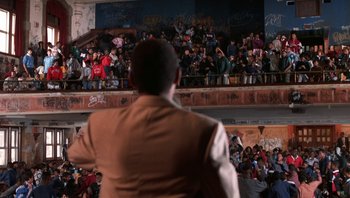 Movie still from “Lean on Me” (1989), directed by John G. Avildsen – A man standing in front of a crowd of onlookers; Extreme Wide shot, High angle