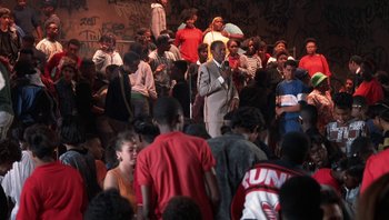 Movie still from “Lean on Me” (1989), directed by John G. Avildsen – A crowd of people standing around a building; Wide shot, High angle