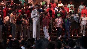 Movie still from “Lean on Me” (1989), directed by John G. Avildsen – A group of people standing on a stage with a microphone; Wide shot, High angle