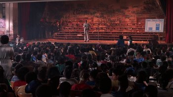 Movie still from “Lean on Me” (1989), directed by John G. Avildsen – A crowd of people sitting and standing in front of an audience; Extreme Wide shot, High angle