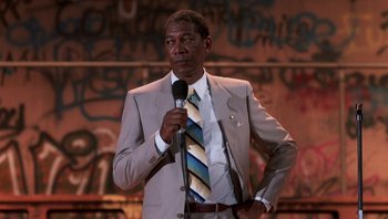 Movie still from “Lean on Me” (1989), directed by John G. Avildsen – A man wearing a suit and tie holding a microphone; Medium shot, Low angle