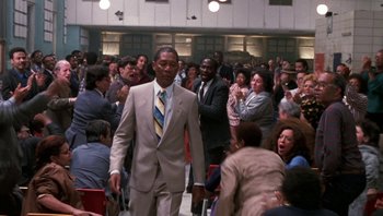 Movie still from “Lean on Me” (1989), directed by John G. Avildsen – A man in a suit walks through a crowd of onlookers; Wide shot, High angle