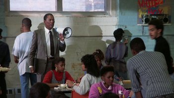 Movie still from “Lean on Me” (1989), directed by John G. Avildsen – A group of people sitting at a table with food; Medium shot, Low angle