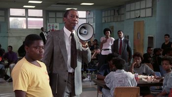Movie still from “Lean on Me” (1989), directed by John G. Avildsen – A man in a suit and tie holding a megaphone; Medium shot, Low angle