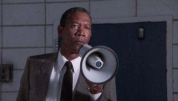 Movie still from “Lean on Me” (1989), directed by John G. Avildsen – A man in a suit holding a megaphone in front of his face; Medium shot, Low angle