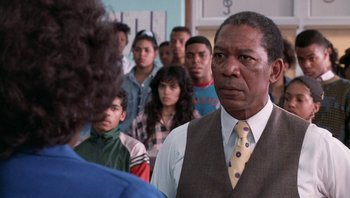 Movie still from “Lean on Me” (1989), directed by John G. Avildsen – An older man in a tie and a group of young people in a room; Close Up shot, Over the shoulder angle