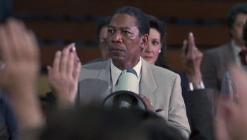 Movie still from “Lean on Me” (1989), directed by John G. Avildsen – A man in a suit and tie sitting next to a woman; Medium shot, Low angle
