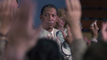 Movie still from “Lean on Me” (1989), directed by John G. Avildsen – A man in a white shirt and tie holding a microphone; Close Up shot, Over the shoulder angle