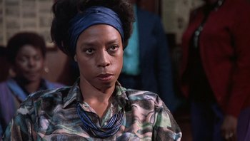 Movie still from “Lean on Me” (1989), directed by John G. Avildsen – A woman wearing a blue head scarf and a green and black patterned shirt; Close Up shot, Low angle