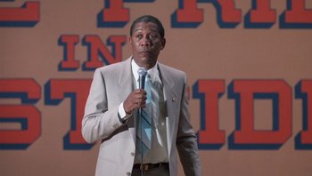 Movie still from “Lean on Me” (1989), directed by John G. Avildsen – A man holding a microphone while standing in front of an audience; Medium shot, Low angle