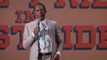 Movie still from “Lean on Me” (1989), directed by John G. Avildsen – A man holding a microphone while standing in front of an audience; Medium shot, Low angle