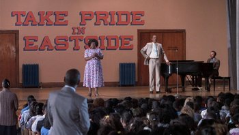 Movie still from “Lean on Me” (1989), directed by John G. Avildsen – A man and a woman on stage in front of an audience; Extreme Wide shot, High angle