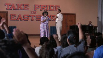 Movie still from “Lean on Me” (1989), directed by John G. Avildsen – A man and a woman standing in front of an audience; Wide shot, Over the shoulder angle