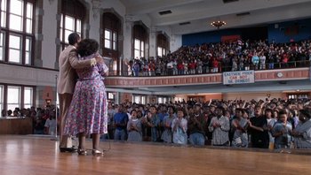 Movie still from “Lean on Me” (1989), directed by John G. Avildsen – A couple of people that are dancing in front of a crowd; Extreme Wide shot, High angle