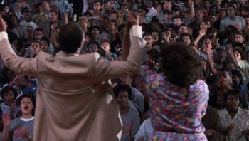 Movie still from “Lean on Me” (1989), directed by John G. Avildsen – A crowd of people sitting and standing in front of a microphone; Medium shot, High angle