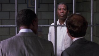 Movie still from “Lean on Me” (1989), directed by John G. Avildsen – A man standing in front of two other men in jail; Medium shot, Over the shoulder angle
