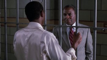 Movie still from “Lean on Me” (1989), directed by John G. Avildsen – A man in a suit and tie standing next to another man in a suit; Medium shot, Over the shoulder angle