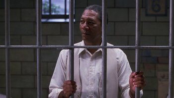 Movie still from “Lean on Me” (1989), directed by John G. Avildsen – A man standing behind bars in a jail cell; Medium shot, Low angle