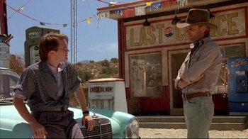 Movie still from “Leatherface: Texas Chainsaw Massacre III” (1990), directed by Jeff Burr – A man and a woman sitting next to each other in front of an old car; Wide shot, Low angle