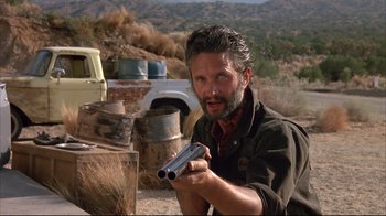 Movie still from “Leatherface: Texas Chainsaw Massacre III” (1990), directed by Jeff Burr – A man holding a gun while standing on a dirt road; Close Up shot, Low angle
