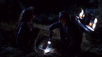 Movie still from “Leatherface: Texas Chainsaw Massacre III” (1990), directed by Jeff Burr – A couple of people sitting on the ground with a flashlight; Medium shot, Low angle