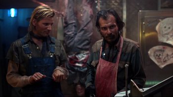 Movie still from “Leatherface: Texas Chainsaw Massacre III” (1990), directed by Jeff Burr – A man with long hair and a beard wearing an apron; Medium shot, Over the shoulder angle