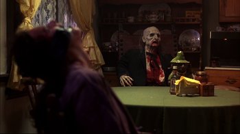 Movie still from “Leatherface: Texas Chainsaw Massacre III” (1990), directed by Jeff Burr – A man in a zombie costume sitting at a table; Medium shot, Over the shoulder angle