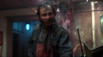 Movie still from “Leatherface: Texas Chainsaw Massacre III” (1990), directed by Jeff Burr – A man in a leather jacket and an apron is smiling; Close Up shot, Low angle