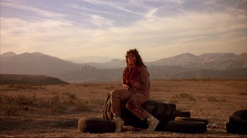 Movie still from “Leatherface: Texas Chainsaw Massacre III” (1990), directed by Jeff Burr – A man sitting on a tire in the middle of a field; Wide shot, Low angle