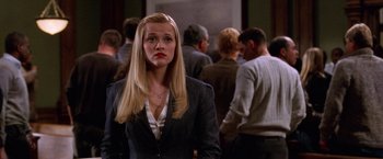 Movie still from “Legally Blonde” (2001), directed by Robert Luketic – A woman with long blonde hair standing in front of a group of people; Medium shot, Over the shoulder angle