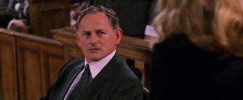 Movie still from “Legally Blonde” (2001), directed by Robert Luketic – A man in a suit and tie sitting in a courtroom; Close Up shot, Over the shoulder angle