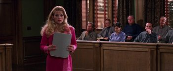Movie still from “Legally Blonde” (2001), directed by Robert Luketic – A woman in a pink dress holding a paper in front of a courtroom; Medium shot, Over the shoulder angle