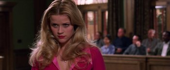 Movie still from “Legally Blonde” (2001), directed by Robert Luketic – A woman in a pink shirt is standing in front of a group of people; Close Up shot, Over the shoulder angle