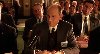 Movie still from “Legally Blonde 2: Red, White & Blonde” (2003), directed by Charles Herman-Wurmfeld – A man in a suit and tie at a microphone; Medium shot, Low angle