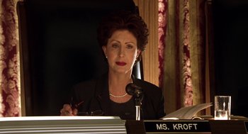 Movie still from “Legally Blonde 2: Red, White & Blonde” (2003), directed by Charles Herman-Wurmfeld – An older woman in a black suit is writing at a microphone; Close Up shot, Low angle