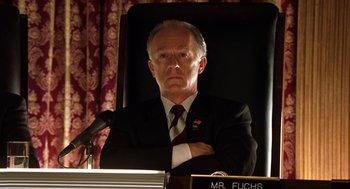 Movie still from “Legally Blonde 2: Red, White & Blonde” (2003), directed by Charles Herman-Wurmfeld – A man in a suit and tie sitting in front of microphones; Close Up shot, Low angle