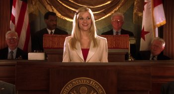 Movie still from “Legally Blonde 2: Red, White & Blonde” (2003), directed by Charles Herman-Wurmfeld – A woman standing at a podium in front of two other people; Medium shot, Low angle