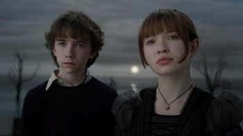 Movie still from “A Series of Unfortunate Events” (2004), directed by Brad Silberling – Two young people standing next to each other in front of the moon; Close Up shot, Low angle