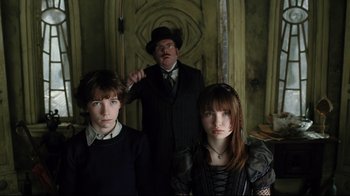 Movie still from “A Series of Unfortunate Events” (2004), directed by Brad Silberling – A man and two women standing next to each other in a room; Medium shot, Low angle