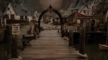 Movie still from “A Series of Unfortunate Events” (2004), directed by Brad Silberling – A wooden bridge leading into a town with a large arch; Extreme Wide shot, High angle