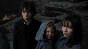 Movie still from “A Series of Unfortunate Events” (2004), directed by Brad Silberling – Three young people standing next to each other in a dark room; Close Up shot, High angle