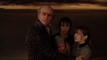 Movie still from “A Series of Unfortunate Events” (2004), directed by Brad Silberling – A man and two women and a child standing next to each other in front of a sunset; Medium shot, Low angle