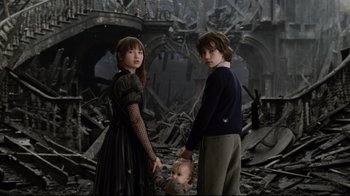 Movie still from “A Series of Unfortunate Events” (2004), directed by Brad Silberling – Two people and a baby standing in the middle of a destroyed room; Medium shot, Low angle