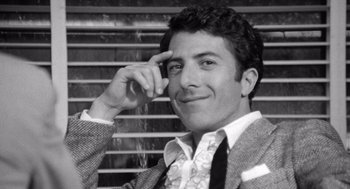 Movie still from “Lenny” (1974), directed by Bob Fosse – A black - and - white photo of a man smiling; Close Up shot, Over the shoulder angle