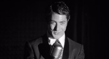 Movie still from “Lenny” (1974), directed by Bob Fosse – A black and white photo of a man holding a microphone; Close Up shot, Low angle