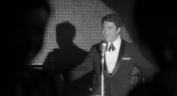 Movie still from “Lenny” (1974), directed by Bob Fosse – A black and white photo of a man in a suit; Medium shot, Over the shoulder angle