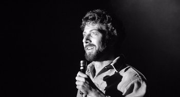 Movie still from “Lenny” (1974), directed by Bob Fosse – Black and white photograph of a man holding a microphone; Close Up shot, Low angle