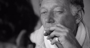 Movie still from “Lenny” (1974), directed by Bob Fosse – An older man smoking a cigar while wearing a ring; Close Up shot, Over the shoulder angle