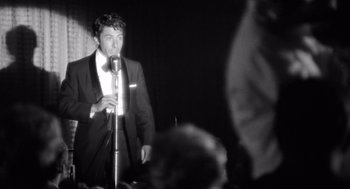 Movie still from “Lenny” (1974), directed by Bob Fosse – A black and white photo of a man singing into a microphone; Medium shot, Low angle